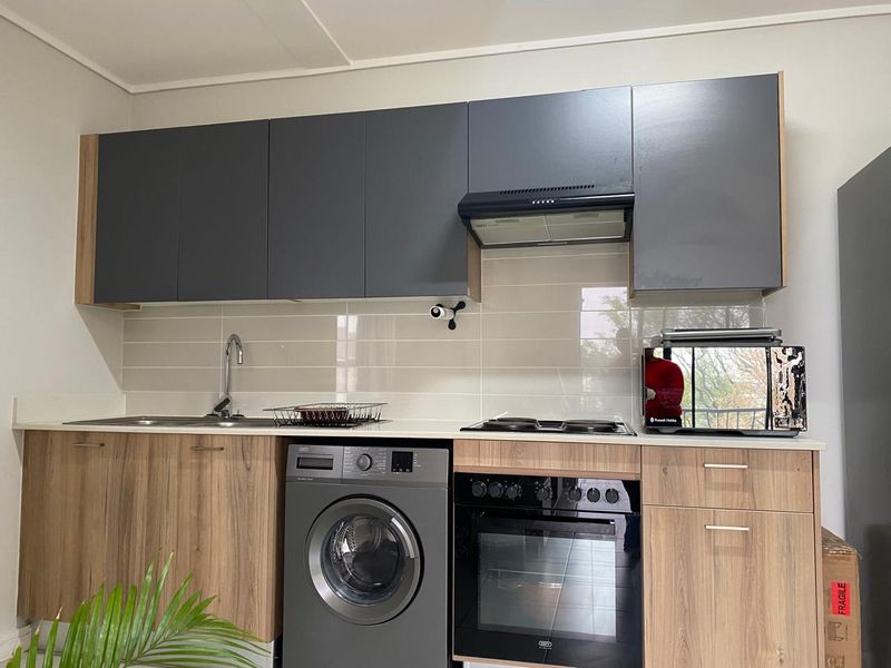 Modern kitchen featuring two-tone cabinetry, integrated oven and hob, extractor fan, tiled backsplash, and a built-in washing machine.