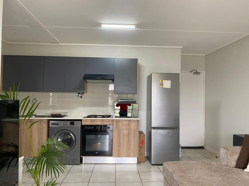 Modern open-plan kitchen featuring dark grey and wood-finish cabinetry, integrated oven and hob, tiled flooring, and a neutral backsplash.