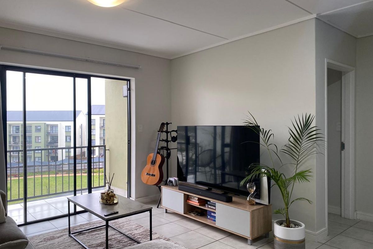A bright living room featuring tiled flooring and a large sliding glass door that opens onto a balcony, providing ample natural light.