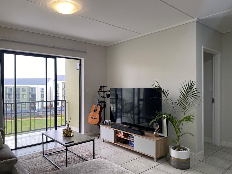 A bright living room featuring tiled flooring and a large sliding glass door that opens onto a balcony, providing ample natural light.