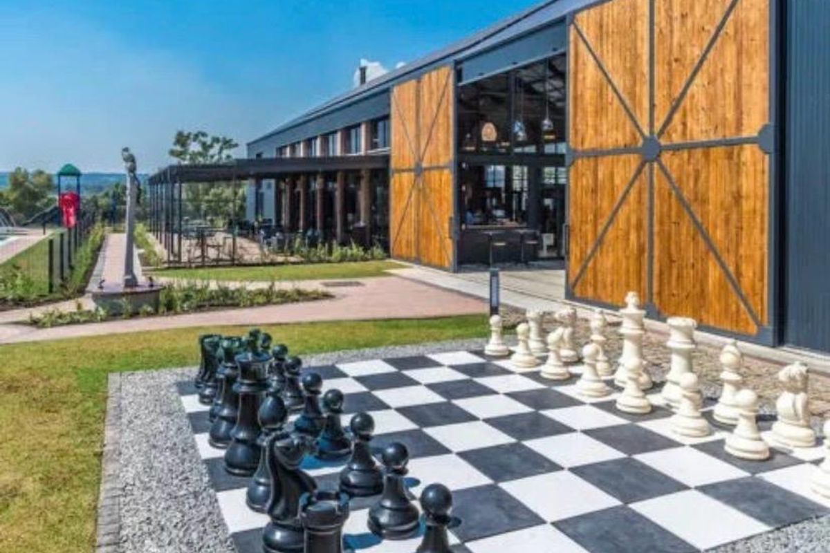 Exterior view of a modern building featuring large sliding wooden barn doors, a landscaped garden, and a permanent outdoor chess set.