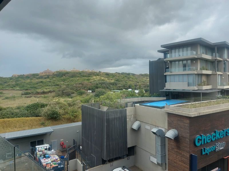 Elevated view overlooking a modern apartment complex with a rooftop swimming pool, metal architectural screening, and surrounding natural landscape.