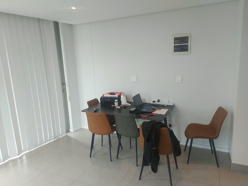 A bright living area featuring neutral tiled flooring, recessed ceiling lighting, and vertical blinds, providing a clean and functional space.
