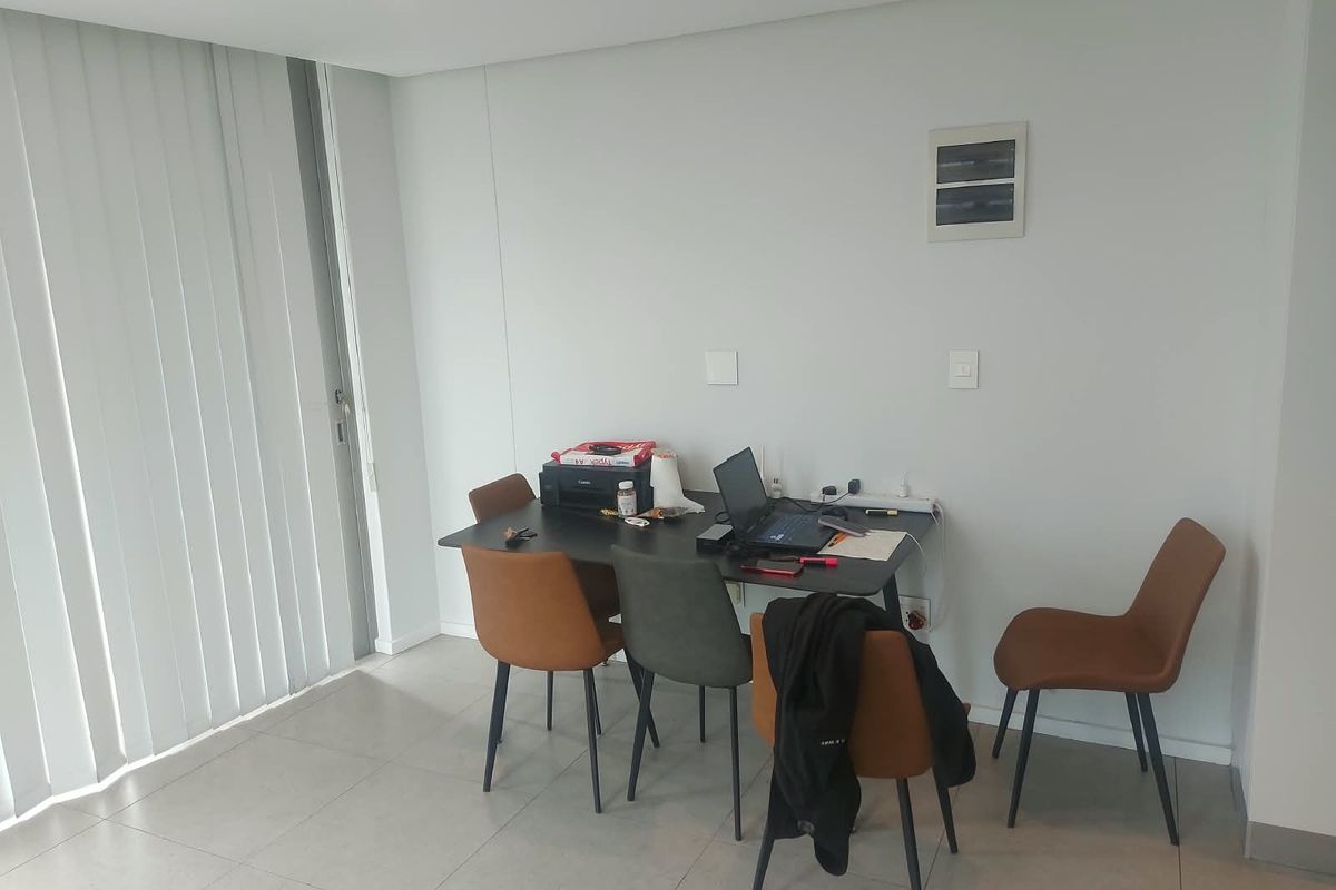 A bright living area featuring neutral tiled flooring, recessed ceiling lighting, and vertical blinds, providing a clean and functional space.