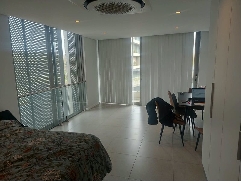 Modern bedroom featuring large floor-to-ceiling glass doors, a sleek glass balustrade, tiled flooring, and integrated ceiling air conditioning.