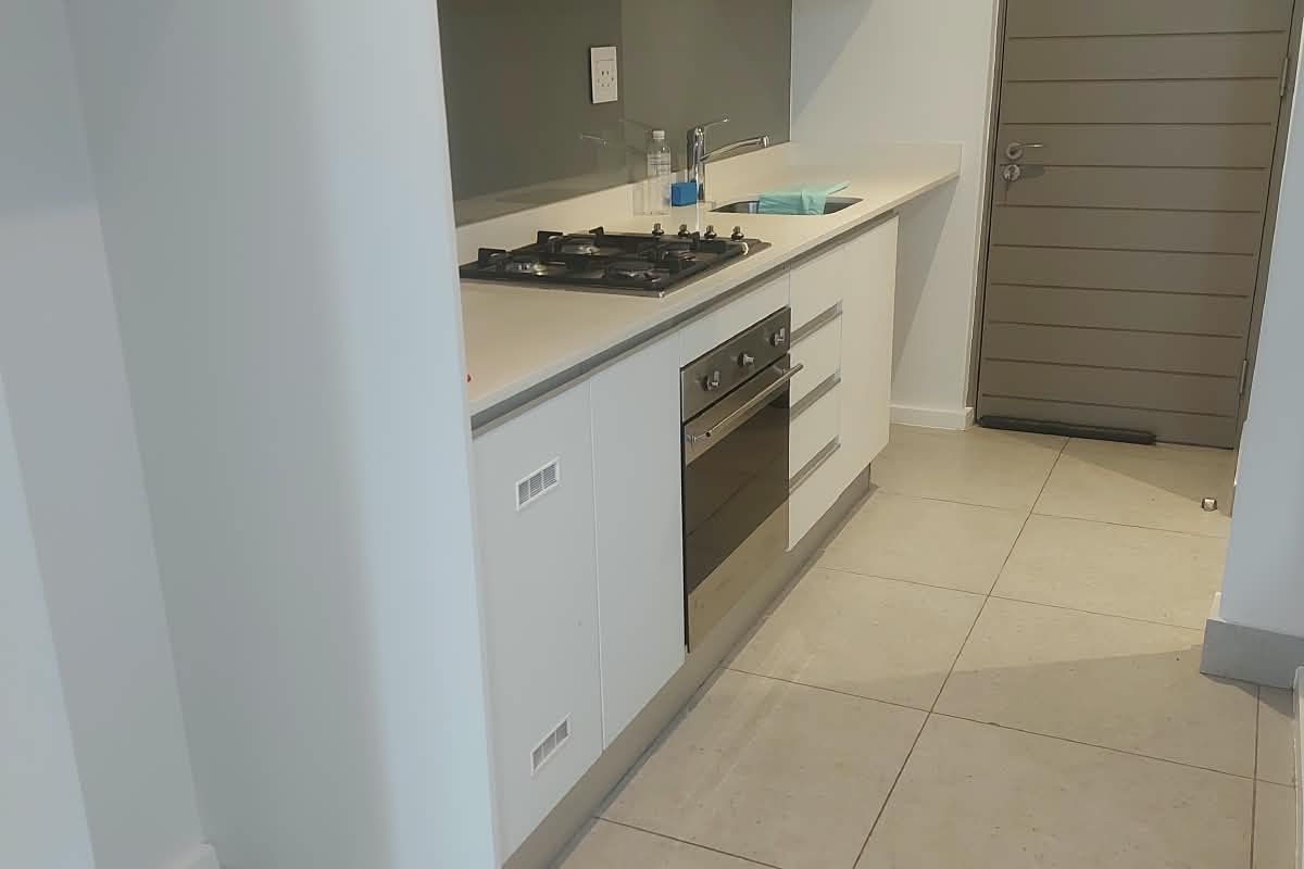 Modern kitchen featuring sleek white cabinetry, stone countertops, a gas hob, built-in oven, and neutral tiled flooring in a clean, minimalist layout.