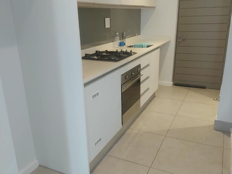 Modern kitchen featuring sleek white cabinetry, stone countertops, a gas hob, built-in oven, and neutral tiled flooring in a clean, minimalist layout.