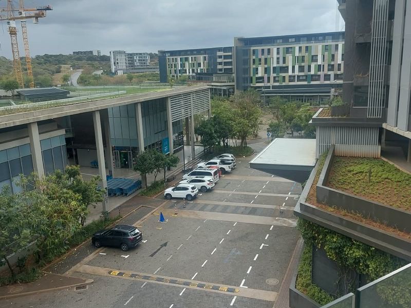 Elevated view overlooking a modern apartment complex, paved parking area, and surrounding landscaped grounds with green roof features.