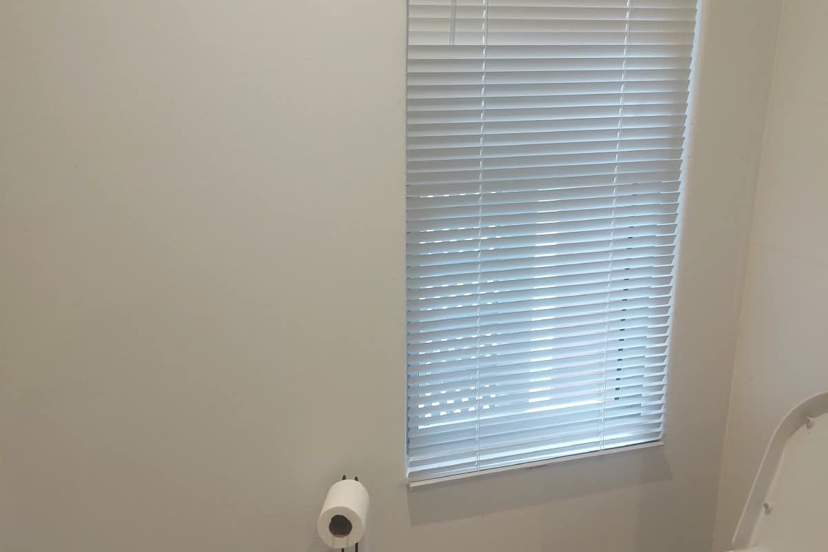 A clean and functional bathroom featuring a toilet, tiled flooring, and venetian blinds for privacy.