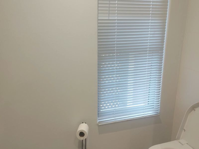 A clean and functional bathroom featuring a toilet, tiled flooring, and venetian blinds for privacy.