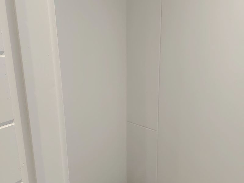 A corner view of a plain interior space with white walls and neutral flooring.