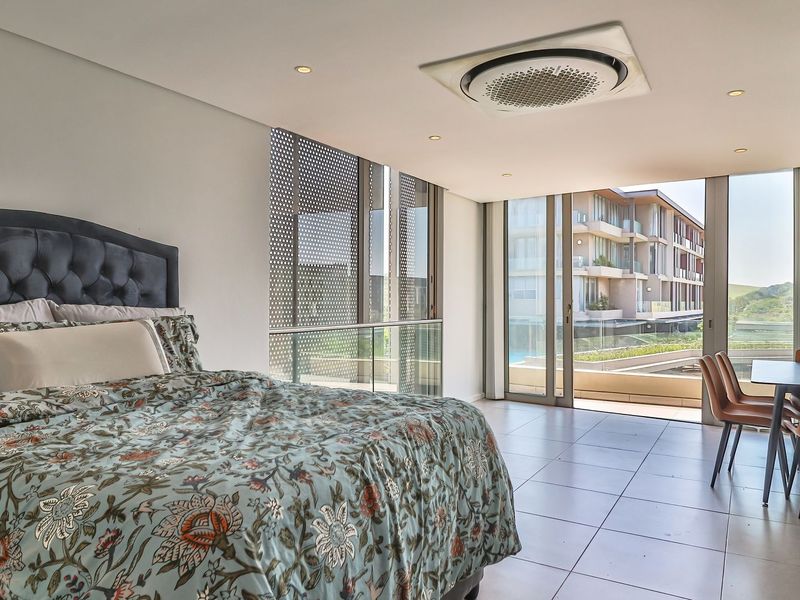 Modern bedroom featuring tiled floors, built-in wardrobes, ceiling-mounted air conditioning, and large sliding glass doors opening to a balcony with a view.