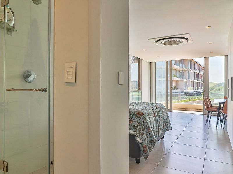 Modern open-plan apartment featuring a sleek glass shower, tiled flooring, integrated ceiling air conditioning, and large sliding doors leading to a private balcony.