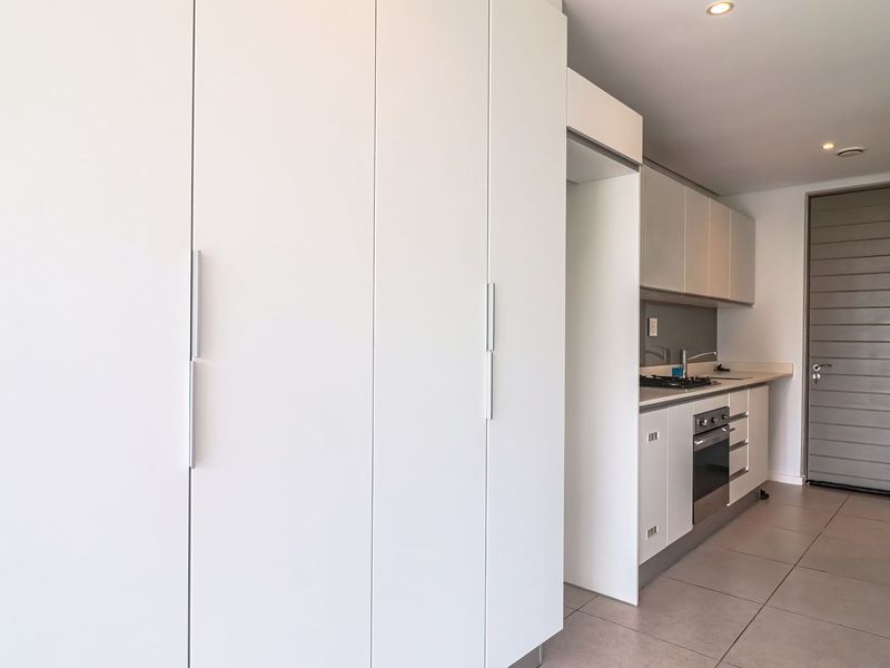 Modern kitchen featuring sleek white built-in cabinetry, integrated oven, hob, and tiled flooring in a clean, minimalist layout.