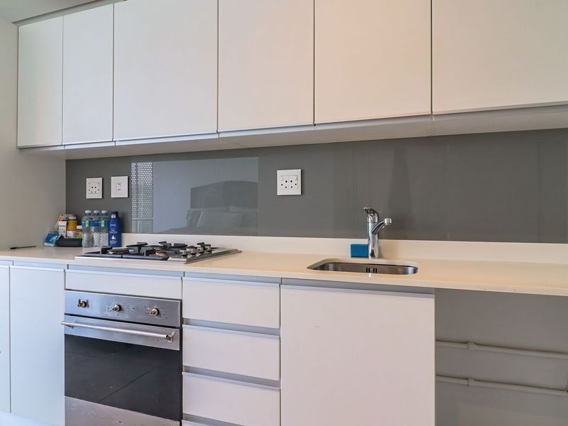 Modern kitchen featuring white cabinetry, stone countertops, a gas hob, built-in oven, and a sleek glass splashback.