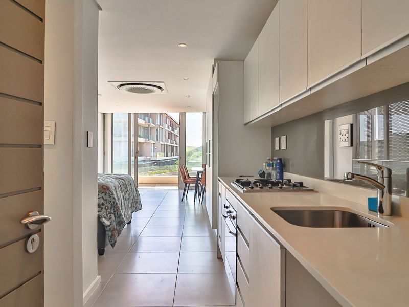 Modern open-plan apartment featuring a sleek kitchen with built-in appliances, tiled flooring, and seamless flow to a bright living area with sliding glass doors.