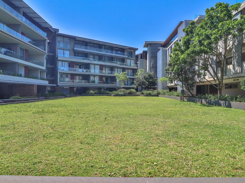 A well-maintained communal garden area surrounded by modern apartment buildings with glass-fronted balconies.