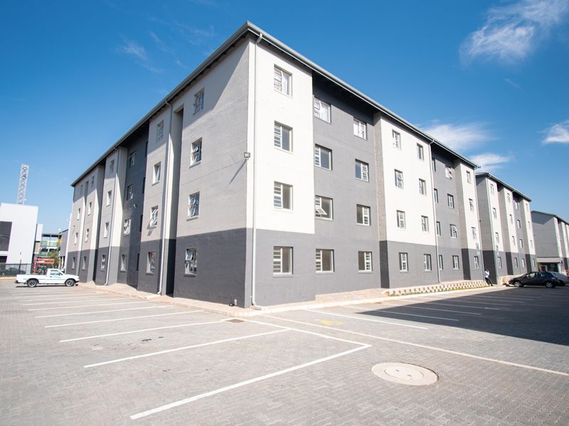 Exterior view of a modern multi-story apartment complex featuring a paved parking lot and clean, contemporary facade finishes.