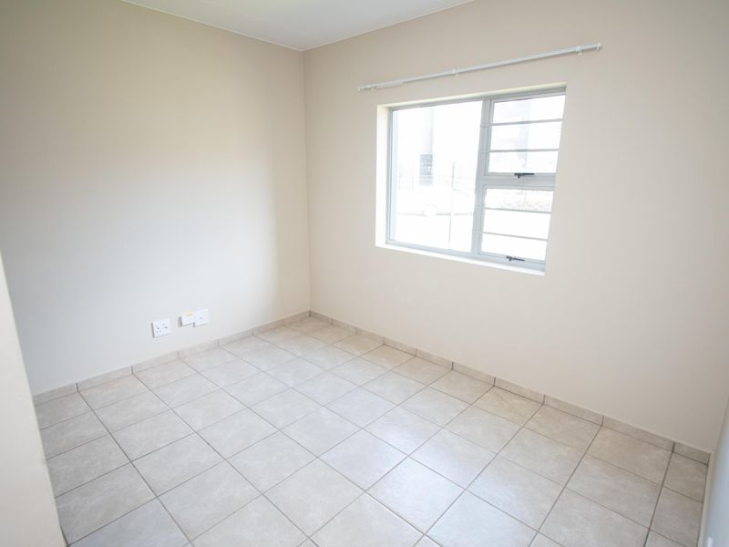 A clean, empty bedroom featuring neutral tiled flooring, a window with security bars, and a curtain rod, ready for personalization.