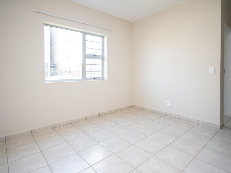 A clean, empty bedroom featuring neutral tiled flooring, a window with security bars, and a simple, well-maintained interior finish.
