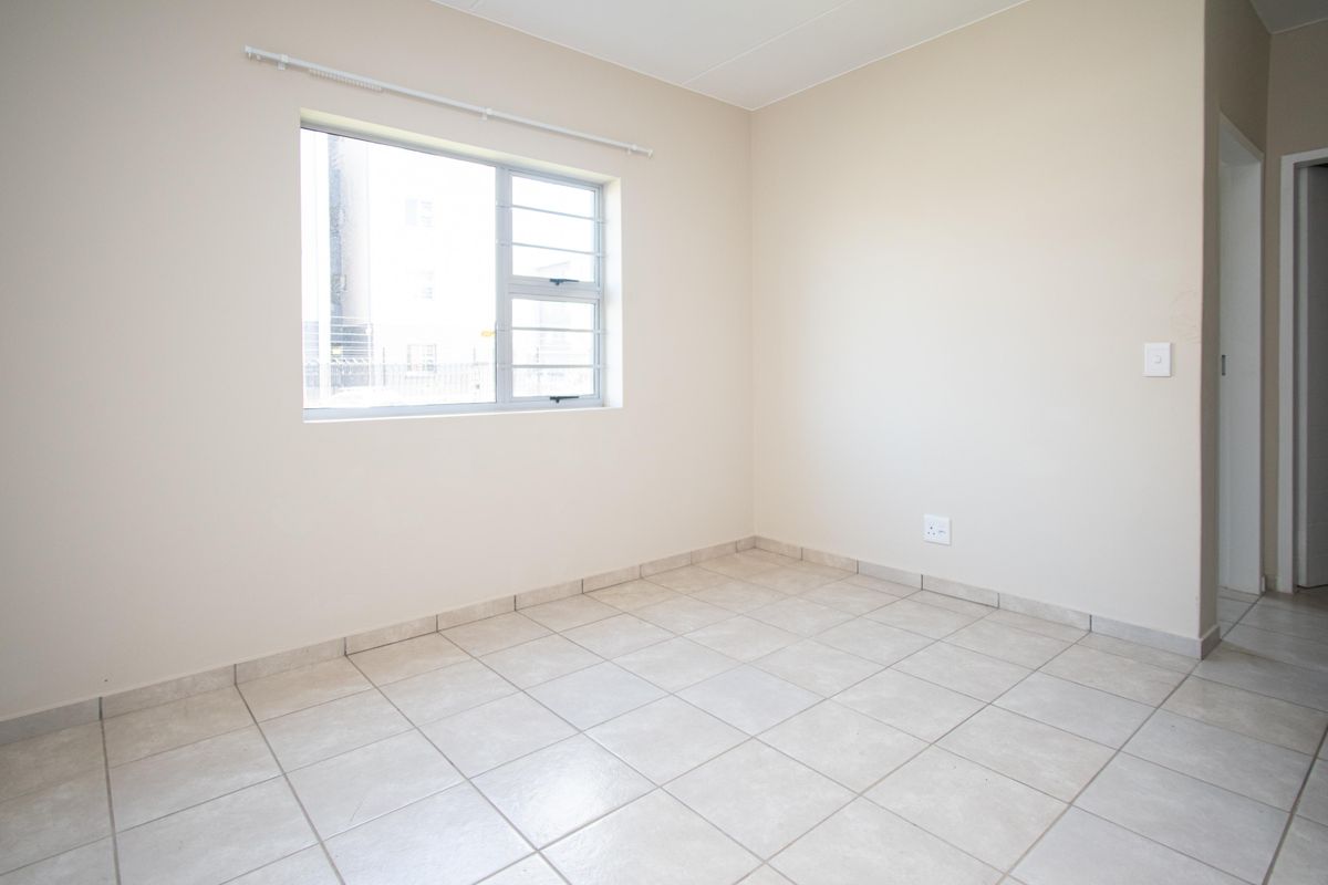 A clean, empty bedroom featuring neutral tiled flooring, a window with security bars, and a simple, well-maintained interior finish.
