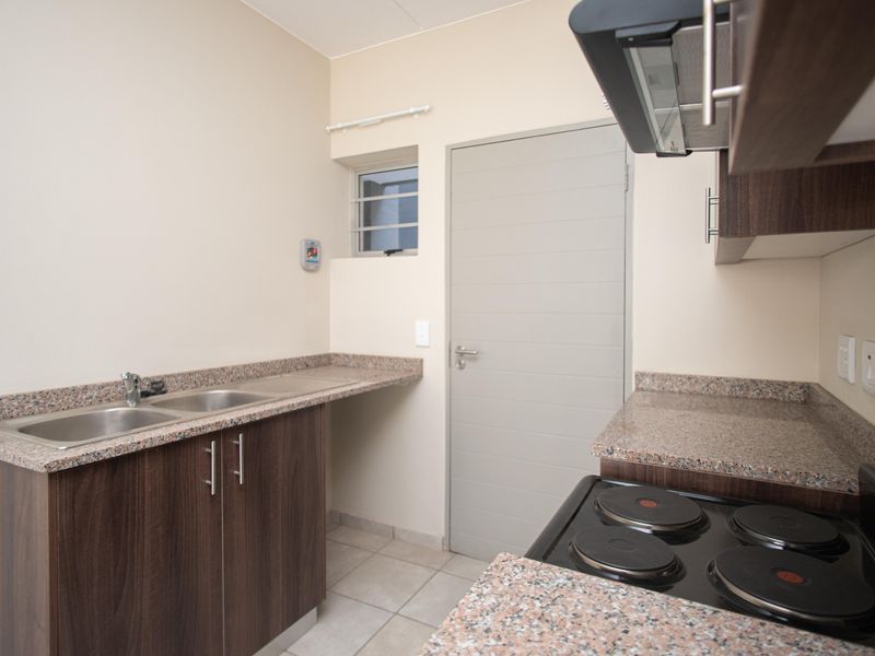 A clean, functional kitchen featuring granite countertops, dark wood cabinetry, a double sink, and a built-in electric hob with an extractor fan.