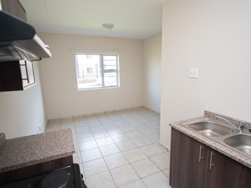 A clean, empty kitchen featuring granite countertops, dark wood cabinetry, a double stainless steel sink, and tiled flooring.