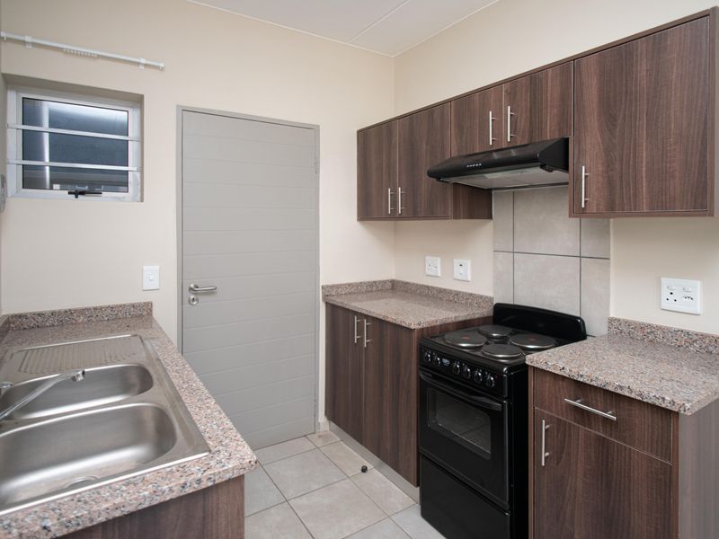 A clean, functional kitchen featuring dark wood-look cabinetry, granite countertops, a double stainless steel sink, and a freestanding electric stove with an extractor fan.