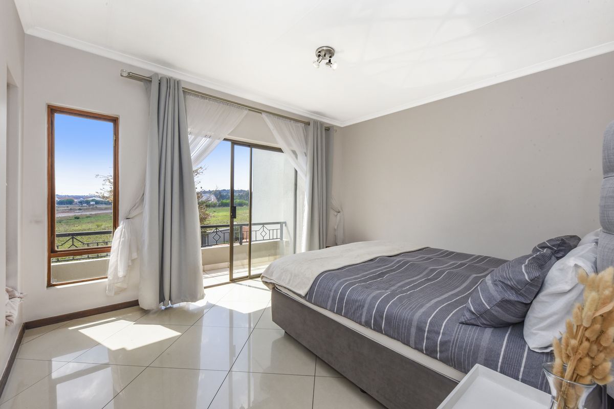 A bright bedroom featuring tiled flooring, a sliding glass door providing balcony access, and neutral wall finishes.