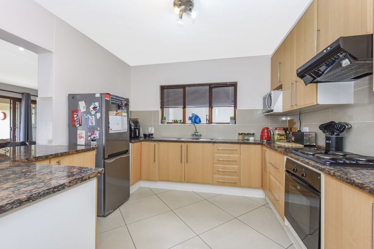 A functional kitchen featuring light wood cabinetry, granite countertops, tiled flooring, and built-in appliances including an oven and hob.