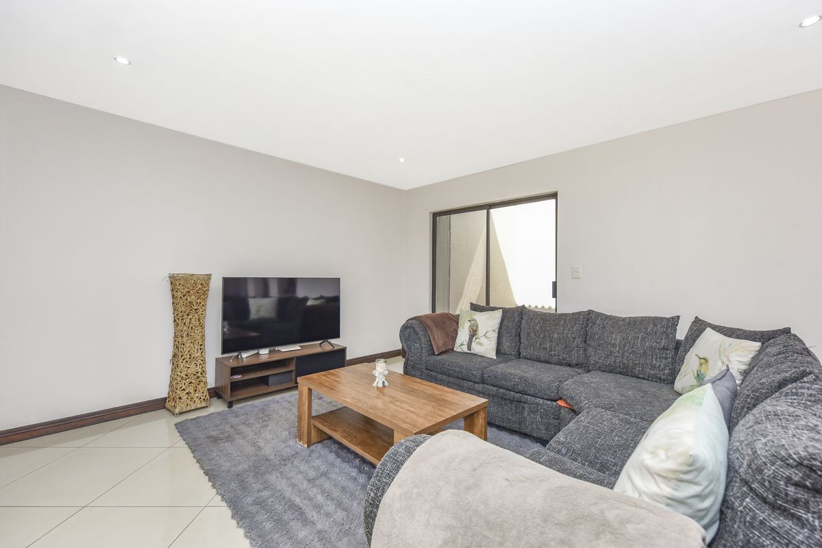 A bright and spacious living room featuring neutral walls, tiled flooring, recessed downlights, and a sliding glass door providing access to the outdoor area.