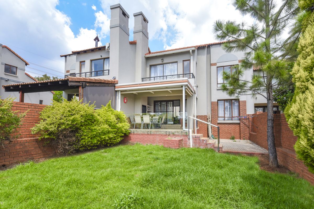 Rear view of the townhouse featuring a private garden, a covered patio area, brick boundary walls, and upper-level balconies with sliding door access.