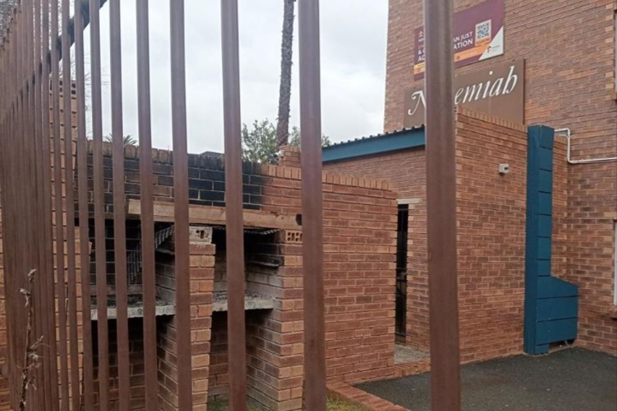 Exterior view of a brick building featuring a built-in brick braai area and security fencing.