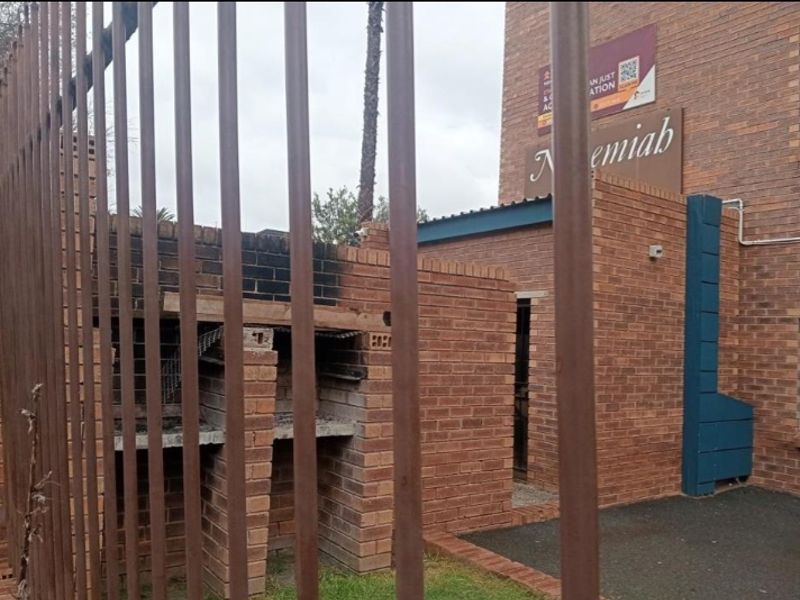 Exterior view of a brick building featuring a built-in brick braai area and security fencing.