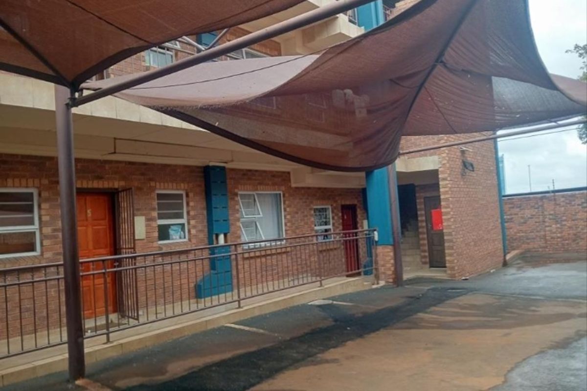 Exterior view of a face brick flat complex featuring a covered carport area and secure metal entrance gates.