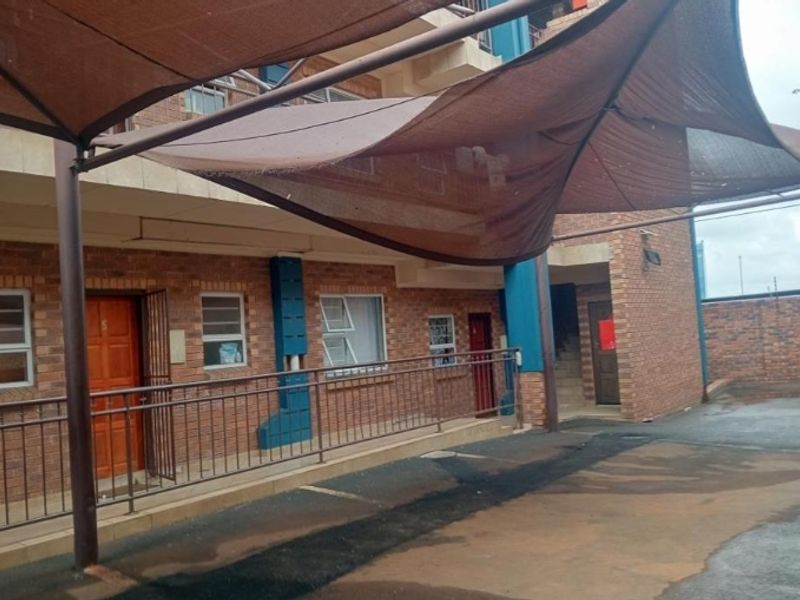 Exterior view of a face brick flat complex featuring a covered carport area and secure metal entrance gates.
