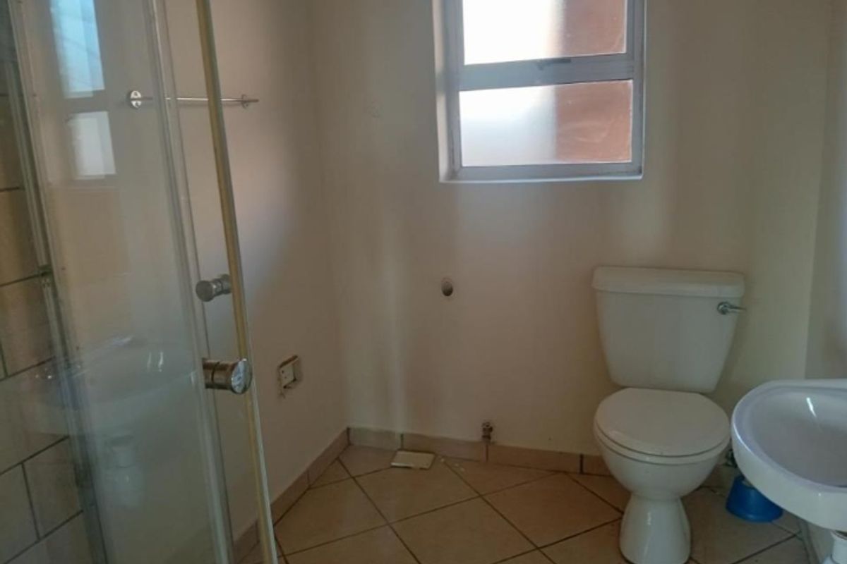 A functional bathroom featuring a shower enclosure, pedestal basin, and toilet, with tiled flooring and a window for natural light.