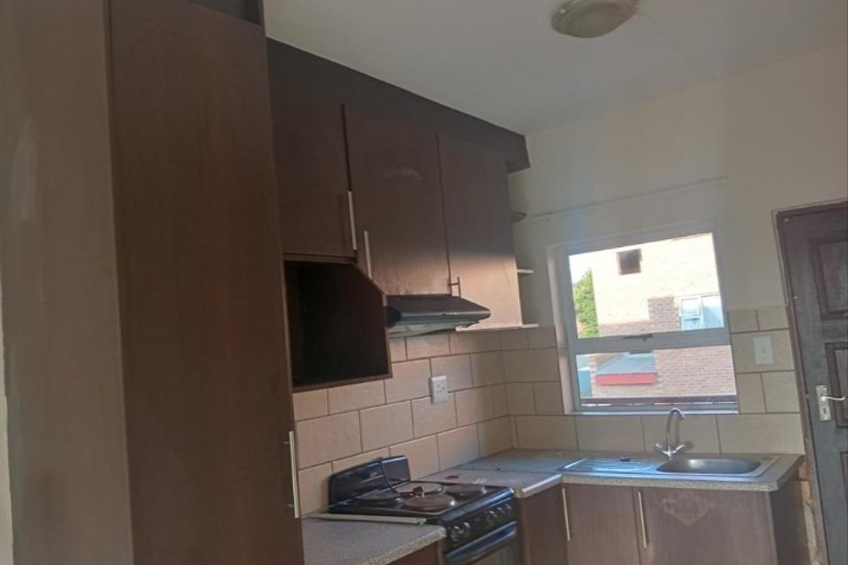 A compact kitchen featuring dark built-in cabinetry, a tiled backsplash, a stainless steel sink, and a built-in stove with an extractor fan.