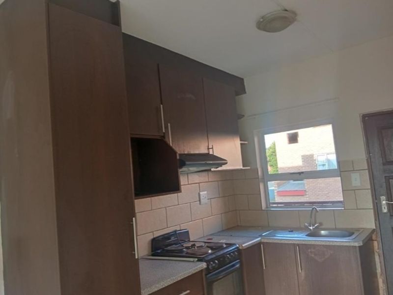 A compact kitchen featuring dark built-in cabinetry, a tiled backsplash, a stainless steel sink, and a built-in stove with an extractor fan.