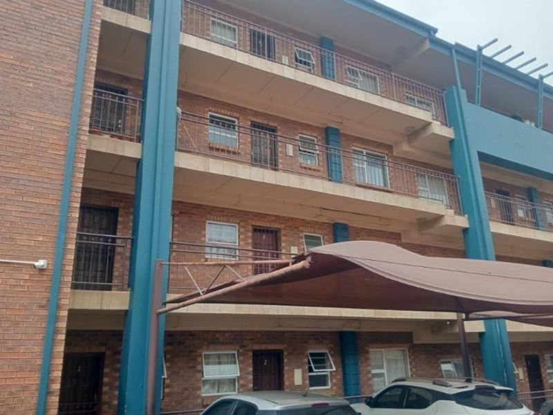 Exterior view of a multi-story brick apartment building featuring private balconies with metal railings and a covered parking area.