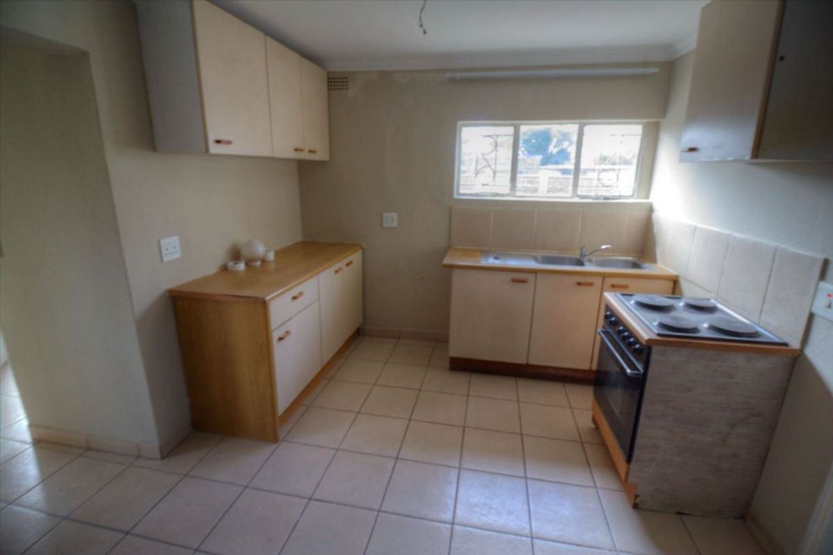 A functional kitchen featuring built-in cabinetry, laminate countertops, a double sink, and an electric stove, with tiled flooring and backsplash throughout.