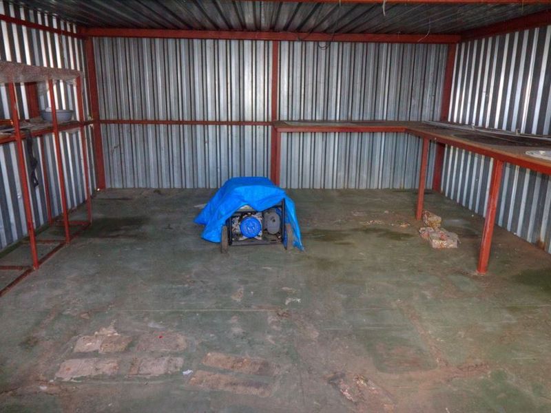 A functional utility space featuring corrugated metal walls, a concrete floor, and a built-in metal workbench, suitable for storage or workshop use.