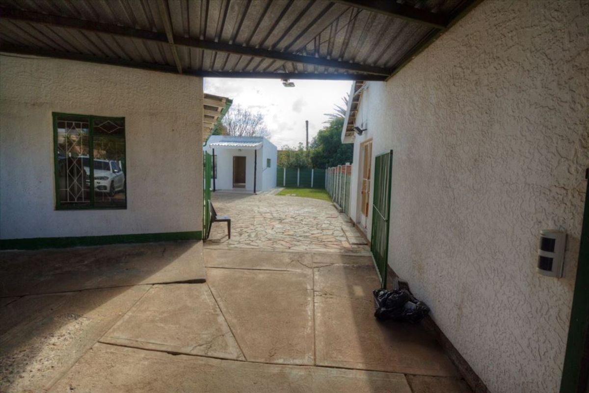 A rear courtyard area featuring a covered patio section, paved flooring, and access to a separate outbuilding structure.