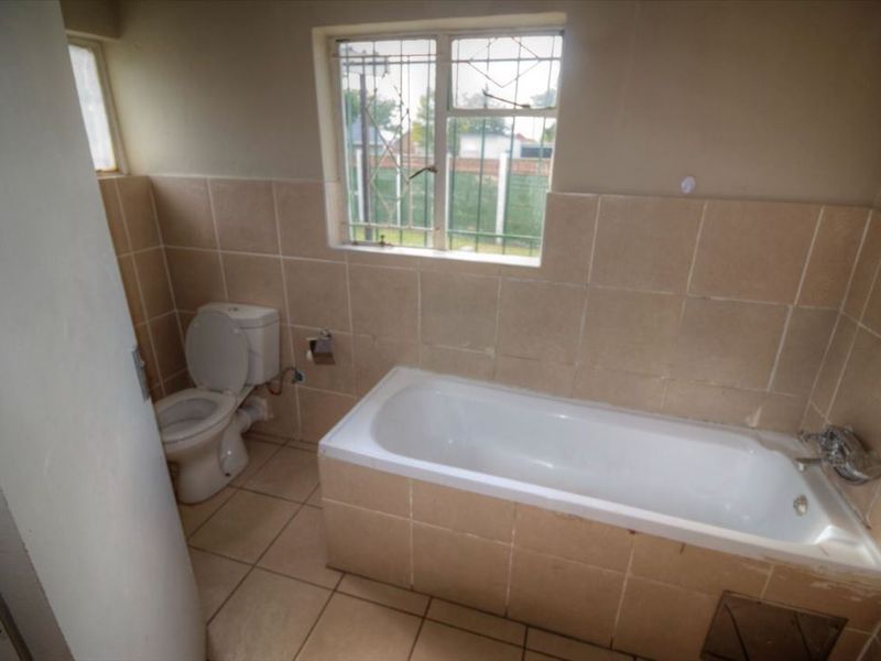 A functional bathroom featuring a standard bathtub, toilet, and neutral wall and floor tiling with security bars on the window.