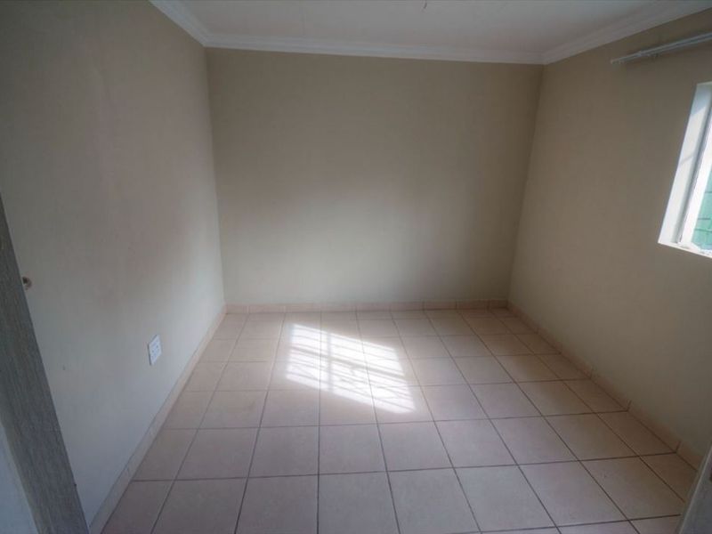A vacant bedroom featuring neutral wall paint, tiled flooring, and a window fitted with security bars.