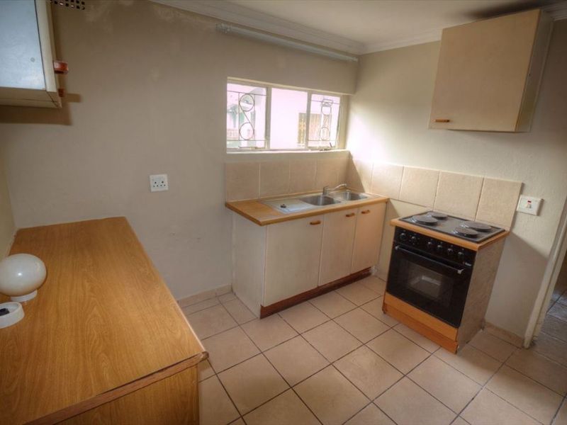 A functional kitchen featuring tiled flooring, built-in cabinetry, a stainless steel sink, and an electric stove with an extractor fan.