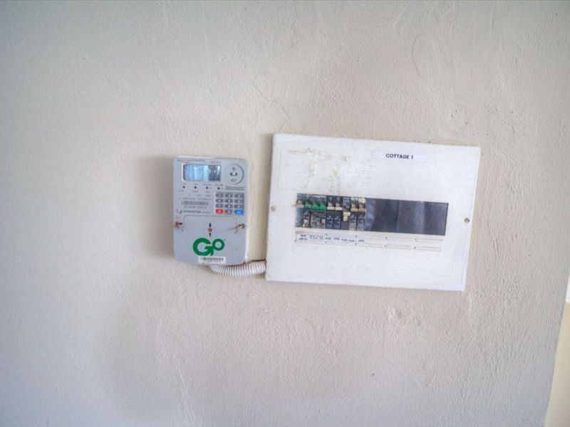 A wall-mounted prepaid electricity meter and electrical distribution board serving the cottage.