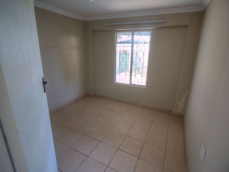 An empty bedroom featuring tiled flooring, neutral walls, and a window fitted with security bars.