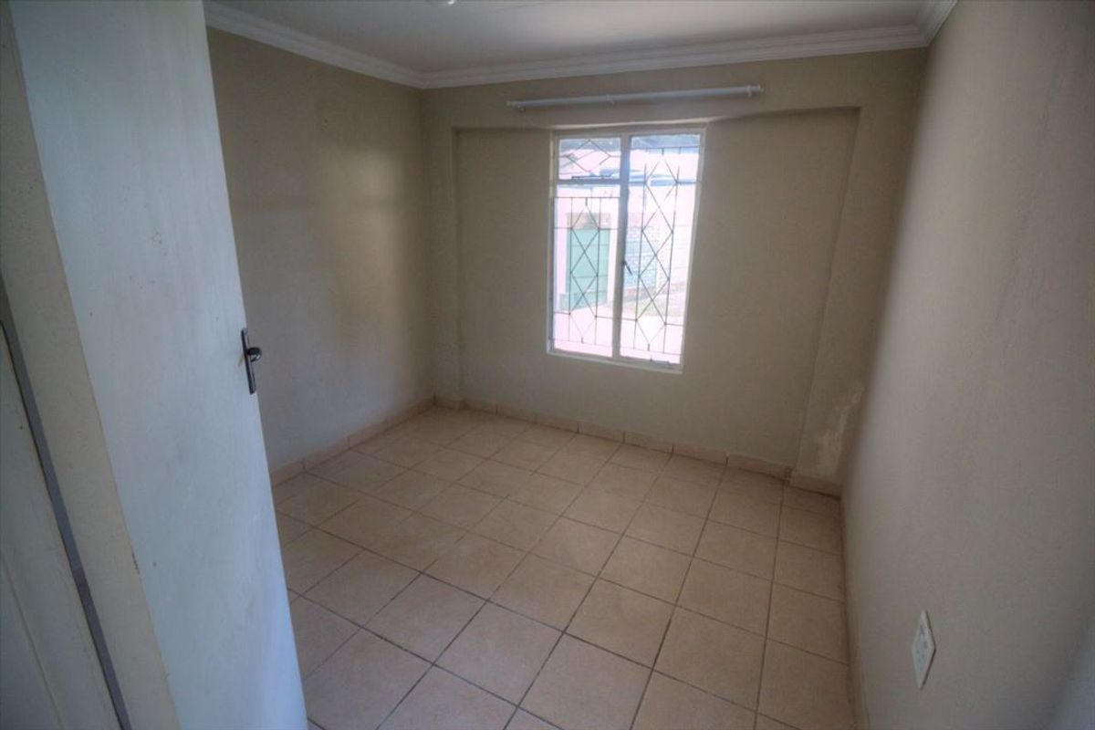 An empty bedroom featuring tiled flooring, neutral walls, and a window fitted with security bars.