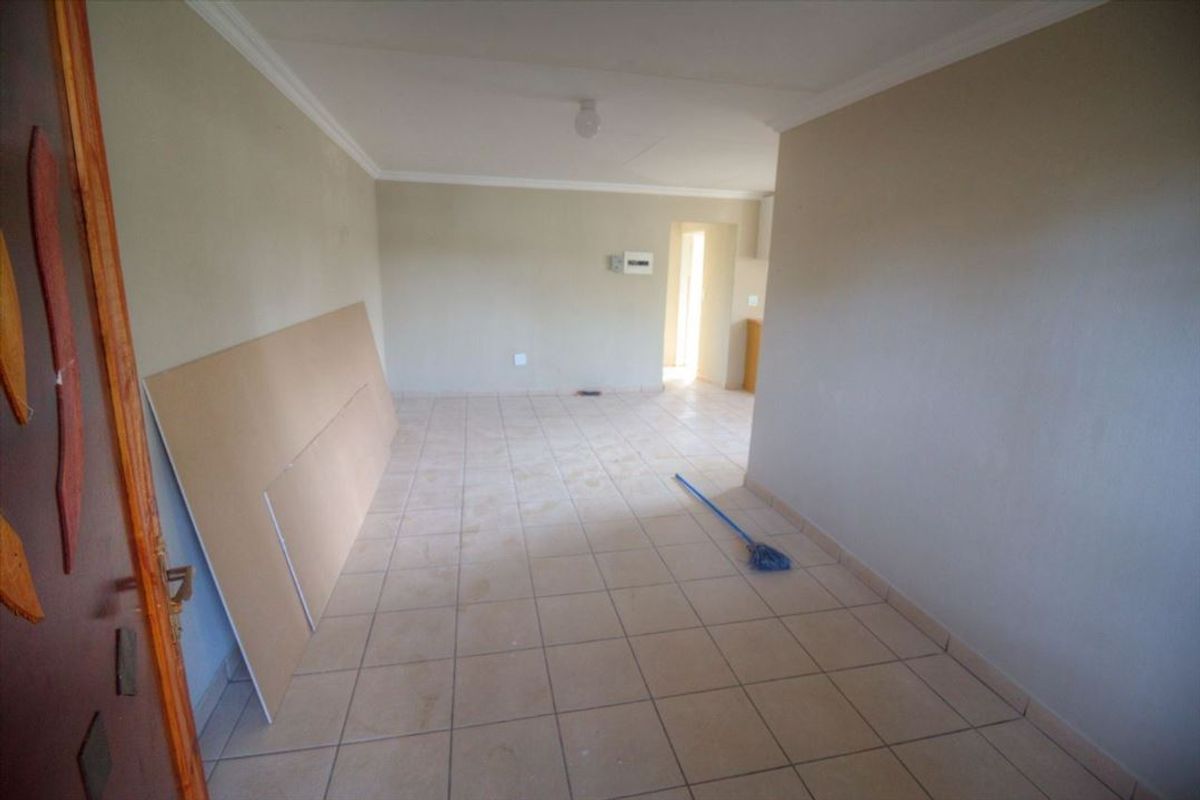 An empty, open-plan living area featuring neutral ceramic floor tiles and coved ceiling cornices, presenting a blank canvas for potential interior design updates.